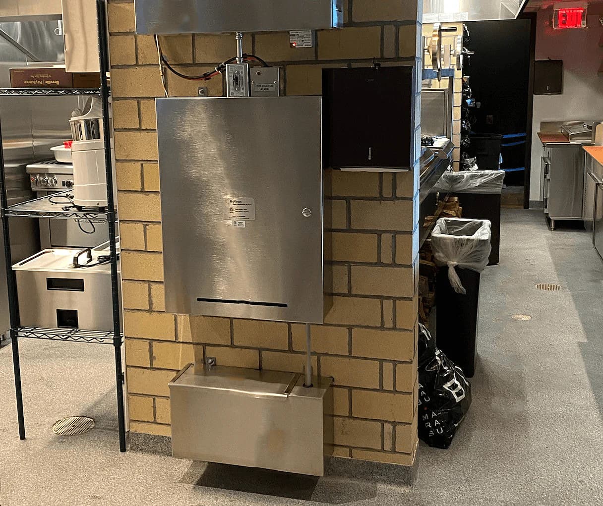 A MOAS cabinet and its solution container installed on a brick wall in a commercial kitchen.